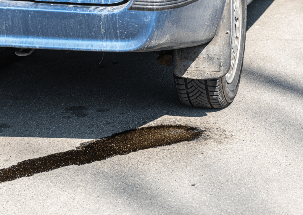 Blue car parked on pavement with a fluid puddle and trail leaking from underneath near rear tire 