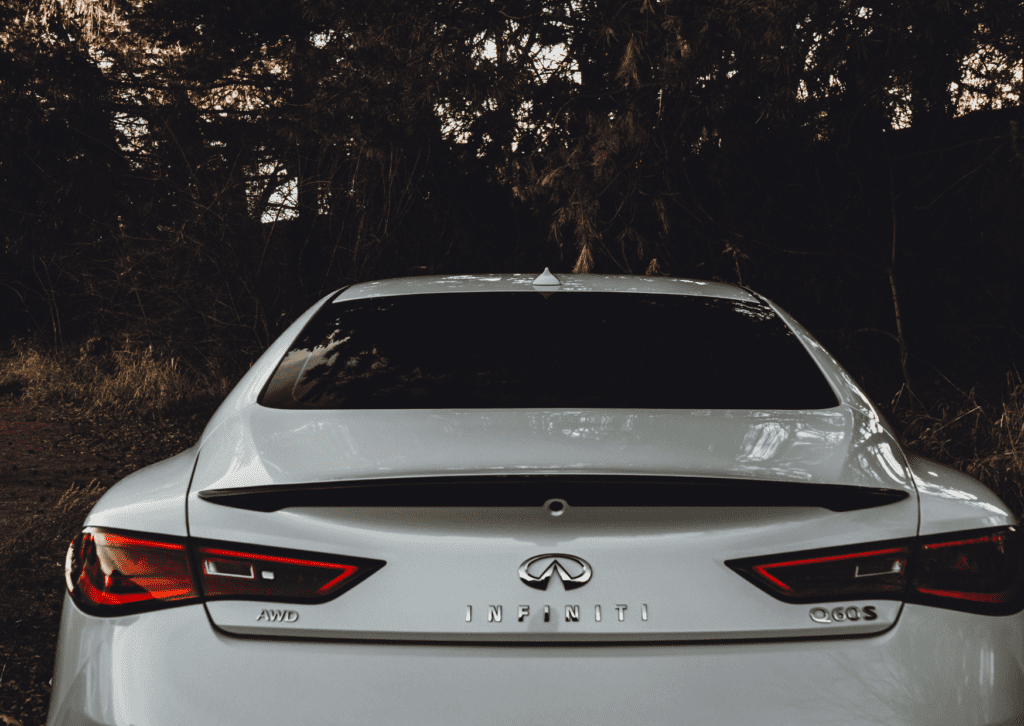 Rear view of white Infiniti sedan showing hybrid and luxury vehicle styling in a wooded area 
