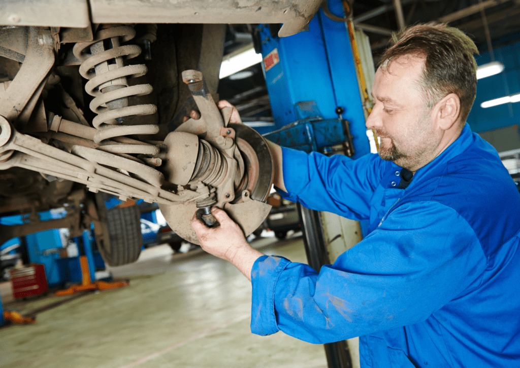 Mechanic inspecting front suspension and brake components on a raised vehicle in the shop bay 