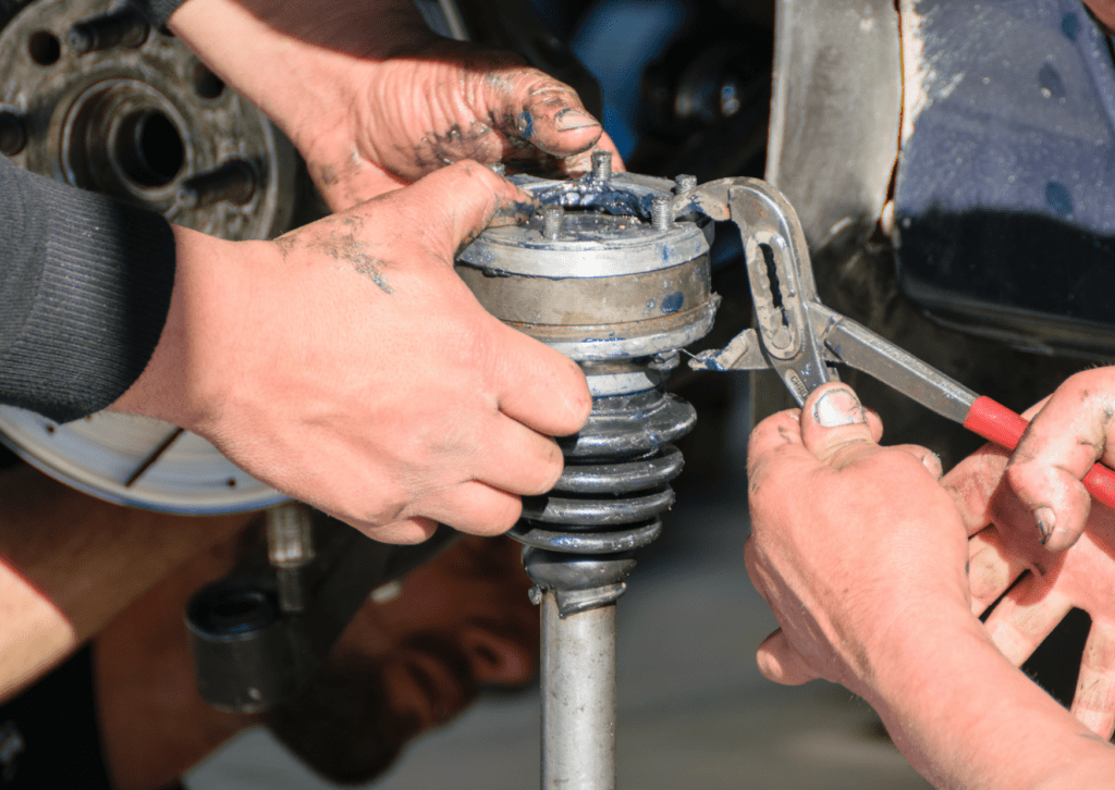 Hands repairing a greasy CV joint and suspension assembly near the wheel hub of a vehicle today 