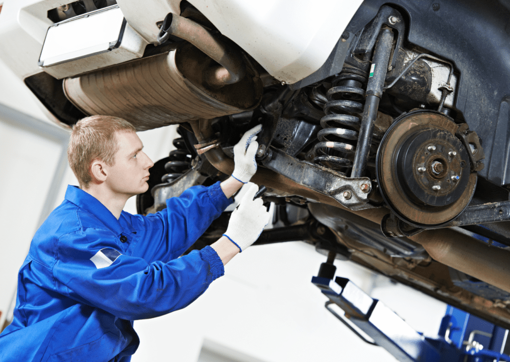 Mechanic inspecting rear suspension parts for suspension-noises-in-car under raised vehicle 
