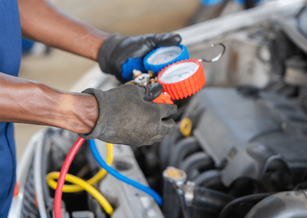 Technician holding AC pressure gauges while testing refrigerant levels inside vehicle engine bay
