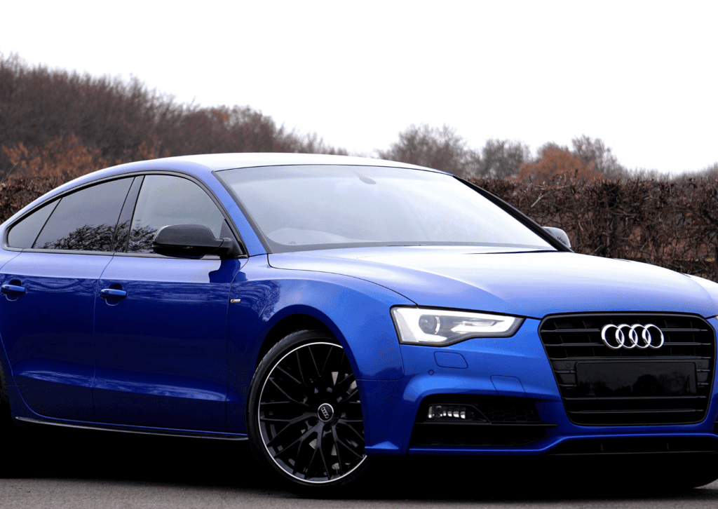 Blue Audi sedan parked outdoors with black wheels, tinted windows, and an autumn backdrop.