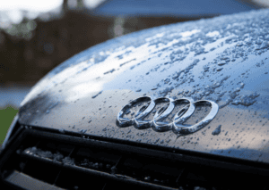 Close-up of chrome Audi rings on a wet hood covered with water droplets and melting ice patches.