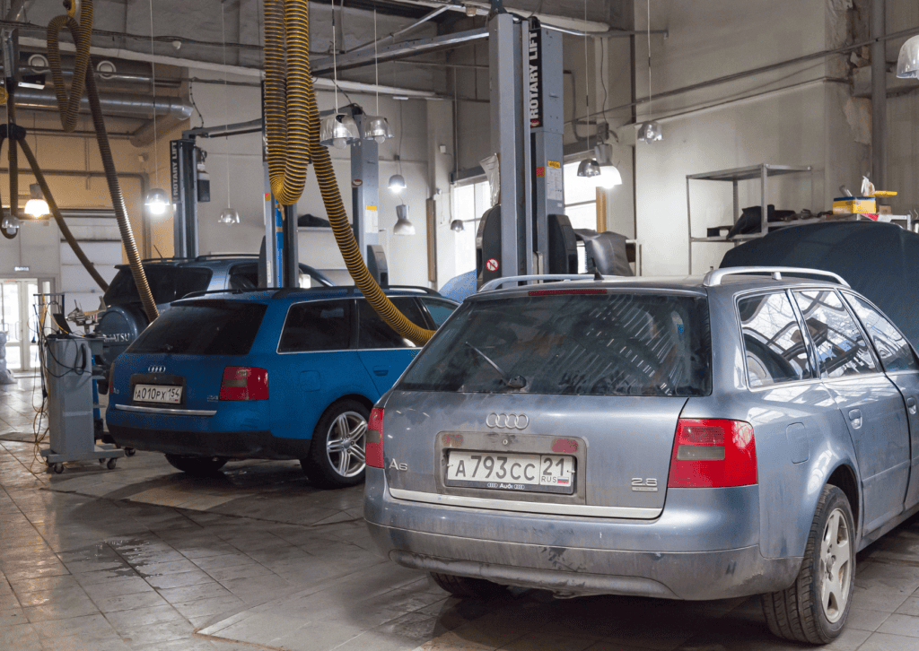 Two Audi station wagons parked inside an auto repair shop with vehicle lifts and service hoses.