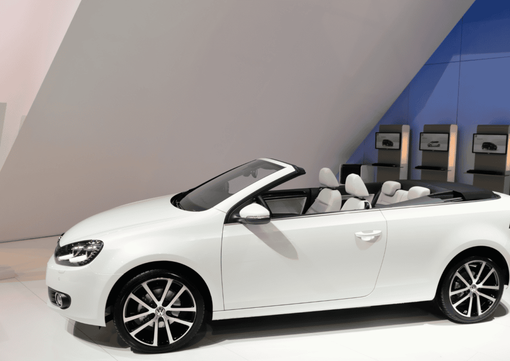 White Volkswagen convertible displayed indoors with its roof down, white seats, and alloy wheels.