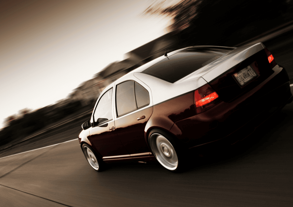 Dark Volkswagen sedan speeding along a curved road with motion blur and glowing rear lights.
