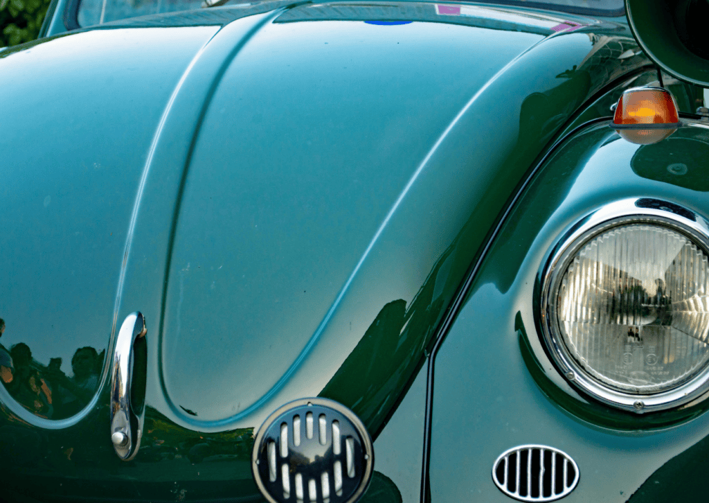Close-up of a vintage green Volkswagen Beetle hood, round headlight, chrome trim, and front grille.