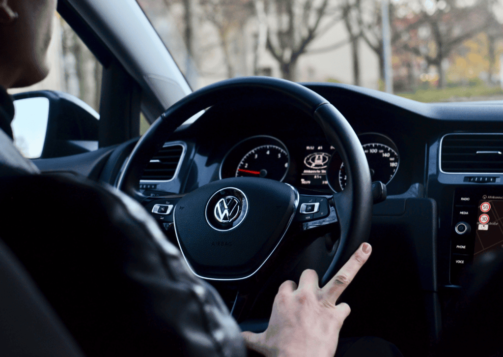 Driver grips the steering wheel inside a Volkswagen while passing through a quiet residential area.