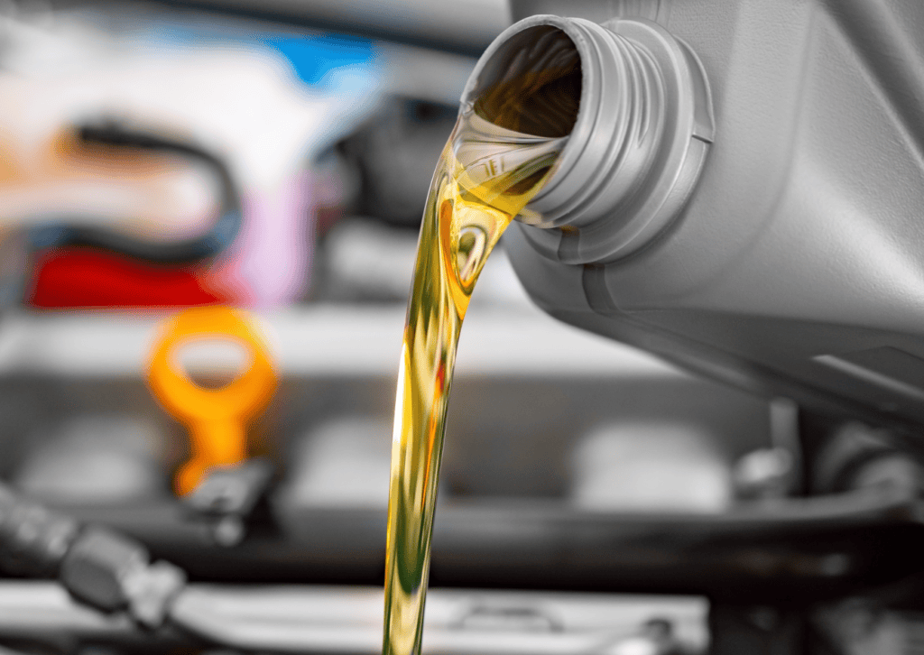 Golden motor oil pouring from a gray bottle into an engine bay during routine vehicle maintenance.