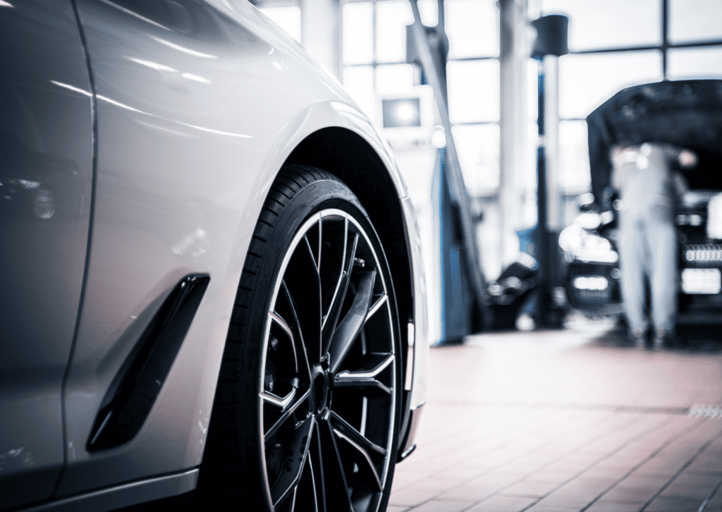 Close-up of a black alloy wheel on a white car inside a bright professional auto repair shop.
