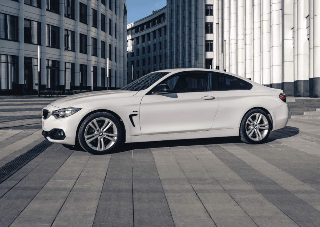 White BMW coupe parked in a modern plaza surrounded by tall contemporary office buildings.
