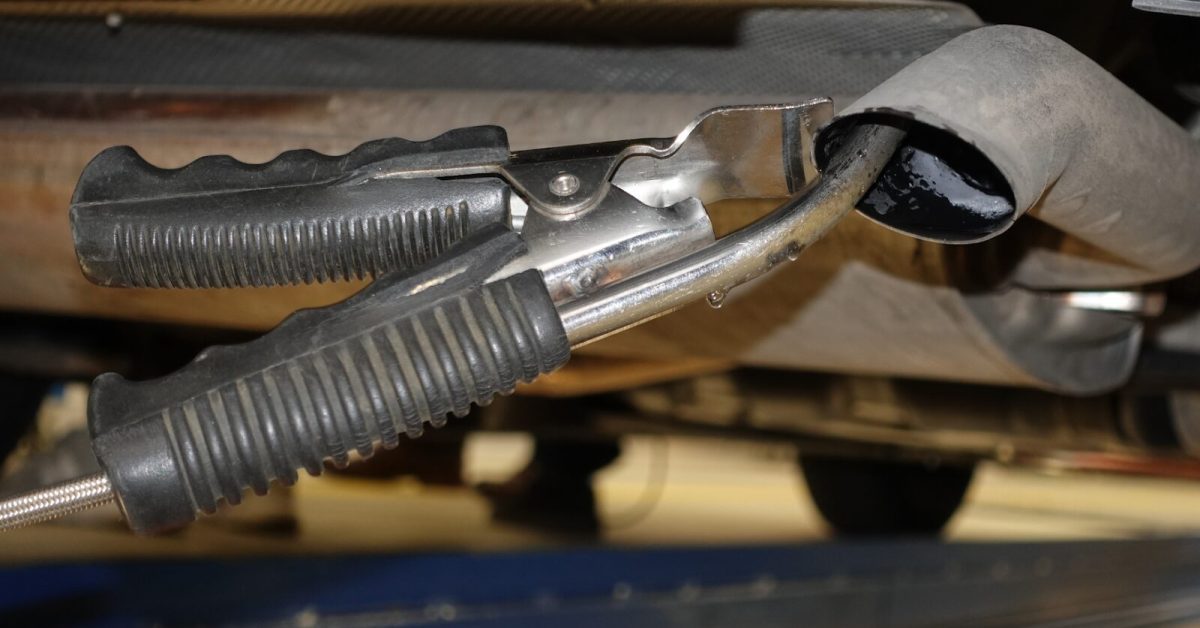 Close-up of a diagnostic tool clamped to a car's exhaust pipe during emission repairs in a workshop