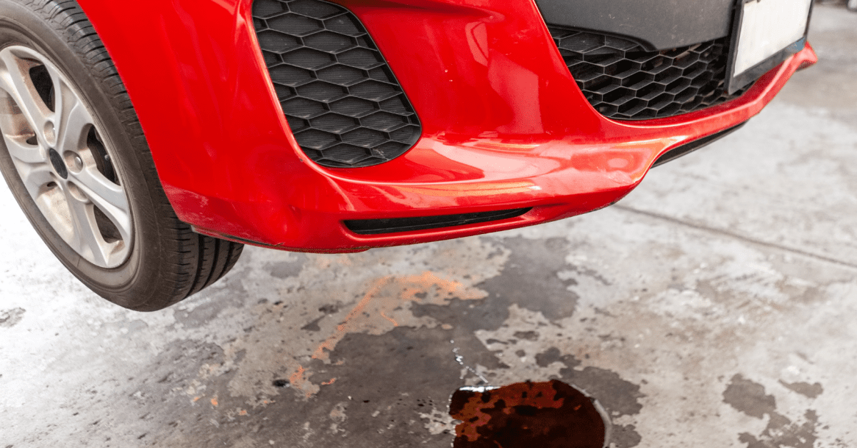 Red car leaking fluid when parked with dark puddle beneath front bumper in repair garage bay 