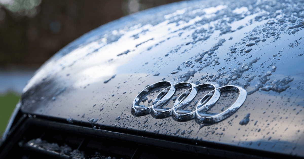 Close-up of chrome Audi rings on a wet hood covered with water droplets and melting ice patches. 