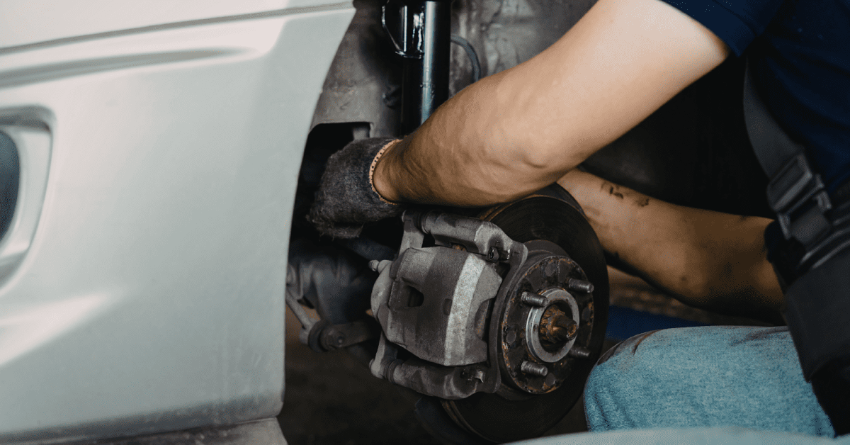 Mechanic repairs front brake and strut to diagnose car suspension noises during service check.