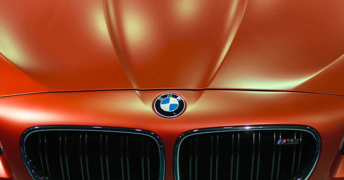 Close-up of a BMW emblem and twin kidney grille on a metallic orange car under showroom lights. 