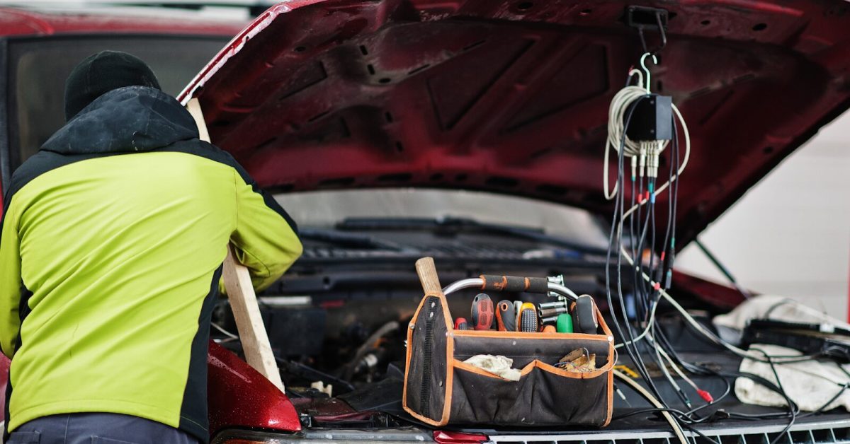 tuneup Mechanic working under the hood of a red truck with tools and diagnostic wires, illustrating what is a tune-up.