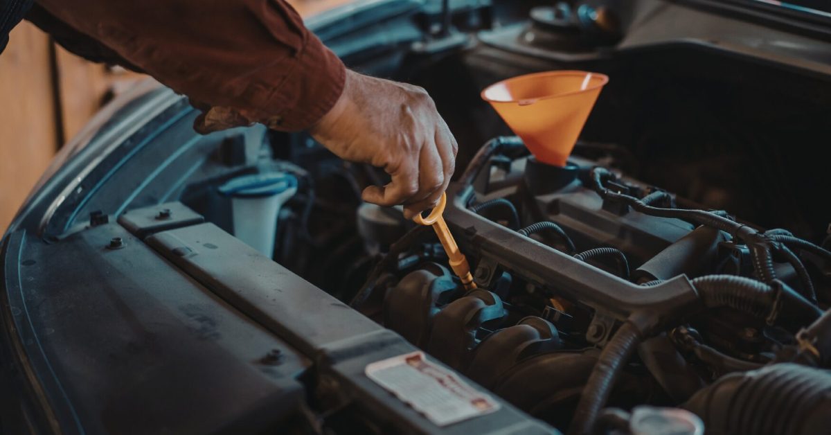 Hand checking engine oil dipstick with funnel in open engine bay for types-of-car-leaks inspection.